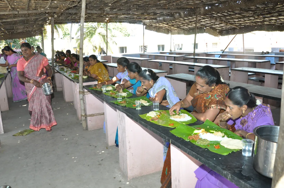 Women trainees seated at long dining tables eating traditional meal on banana leaves