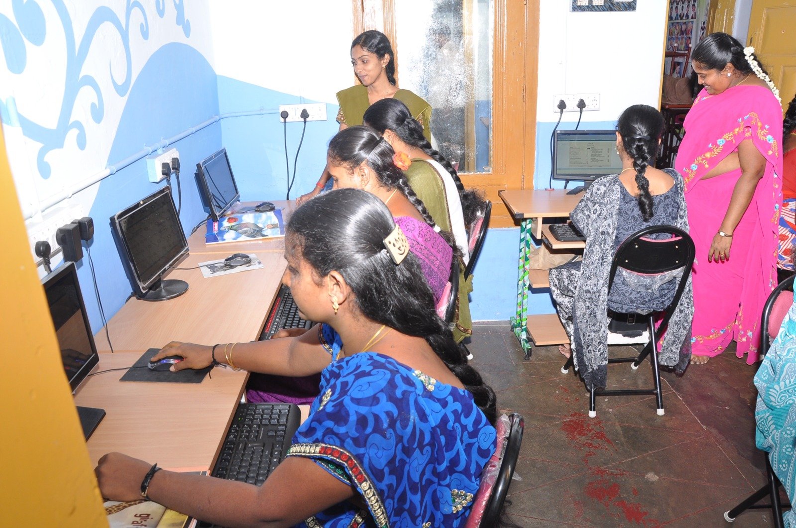 Instructor guiding young women during digital skills and typing practical session